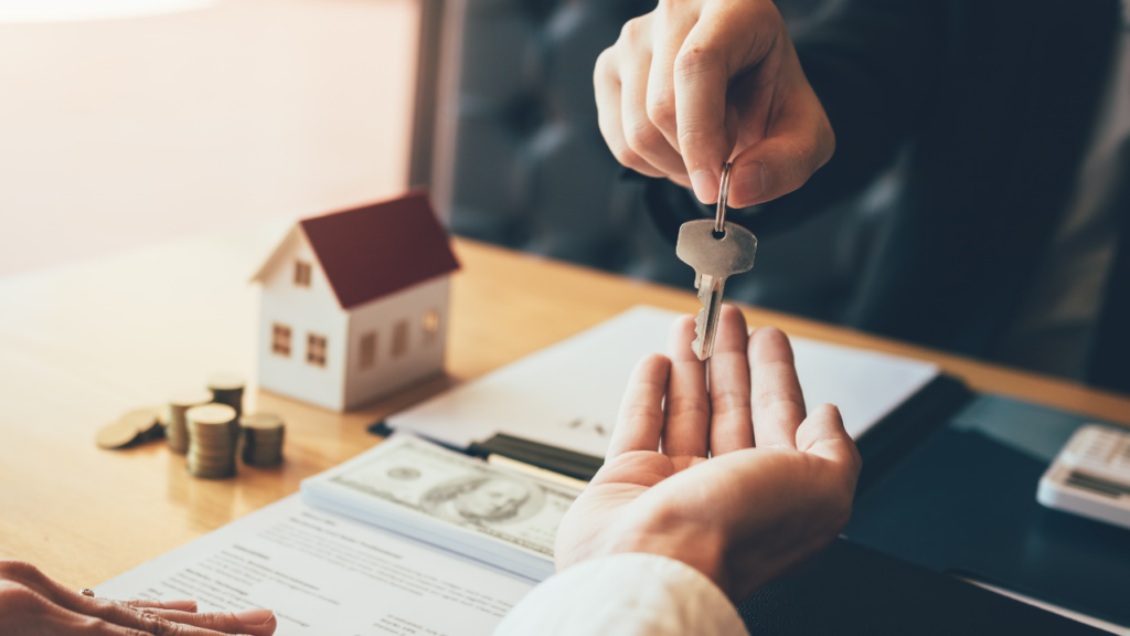 real estate agent handing new house keys to a buyer over the closing tabel