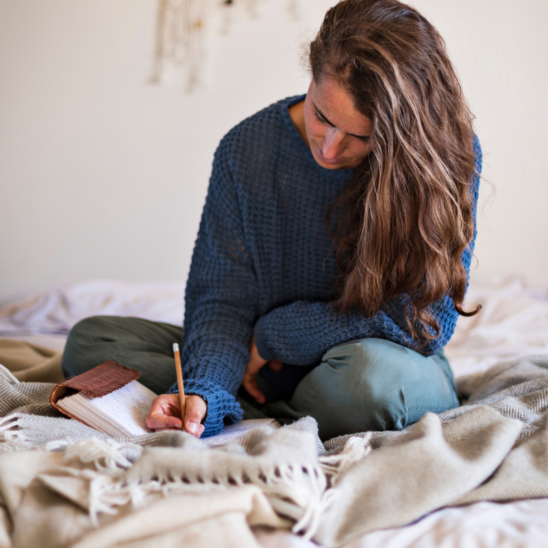 Writing Your Dream Life Vision - Woman sitting on a bed writing in her journal