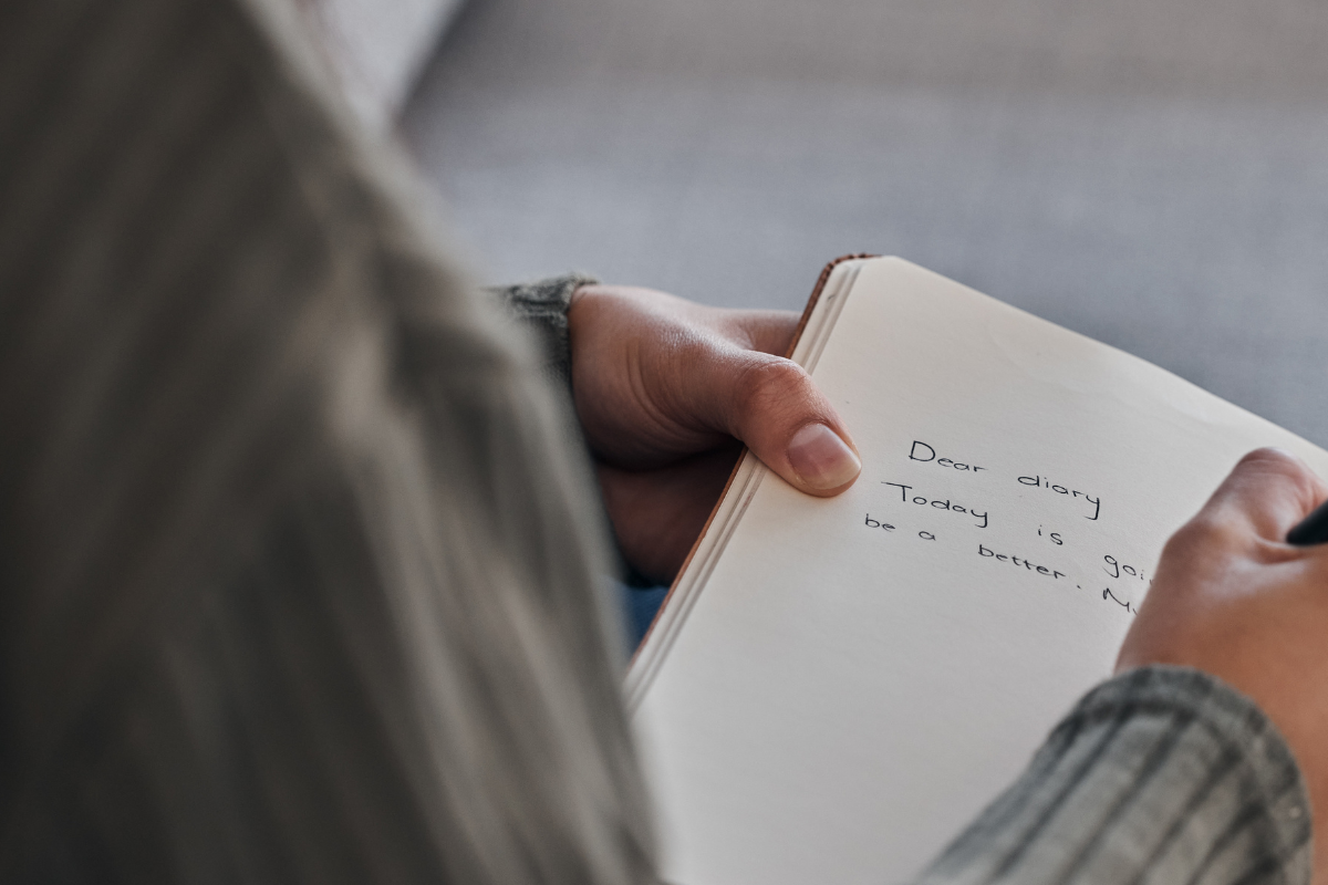 hand-book-and-woman-writing-in-journal-on-a-sofa